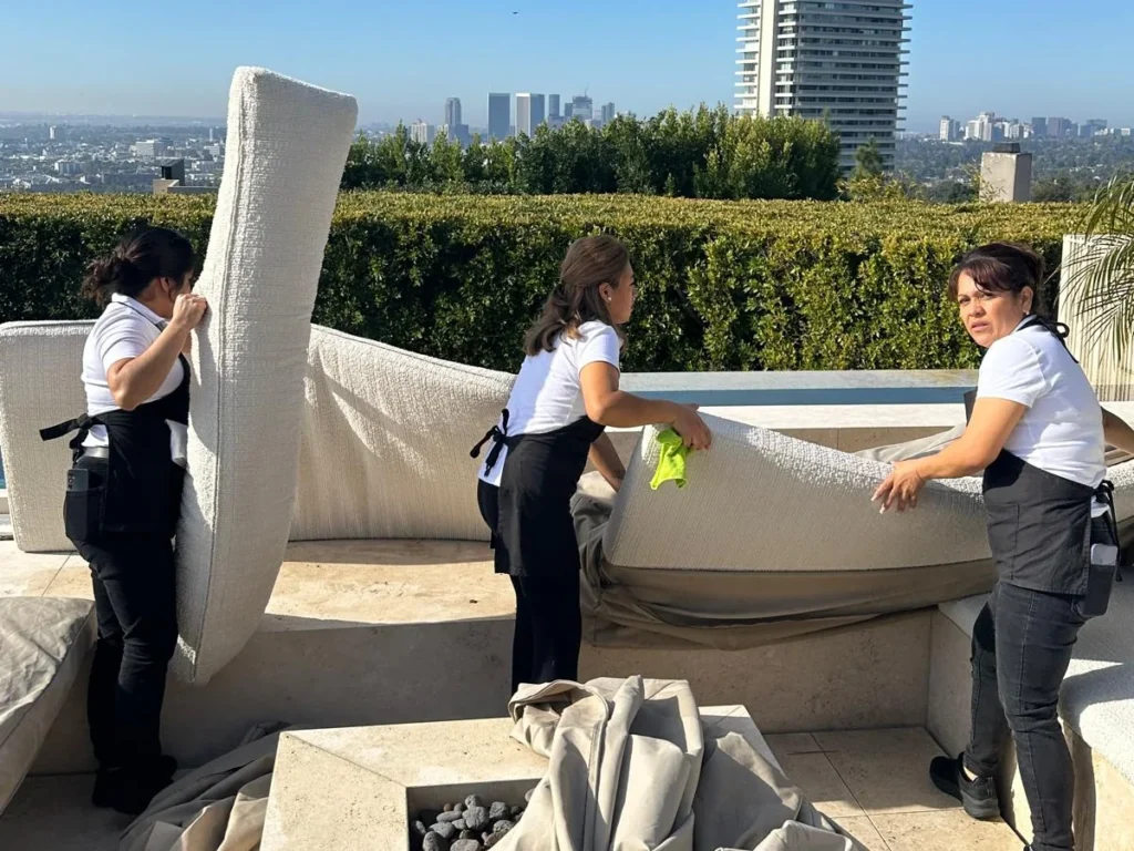 FJ Luxury Services team deep cleaning outdoor sofa cushions on a hillside terrace overlooking Los Angeles